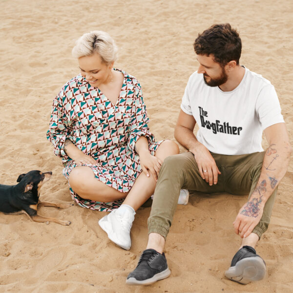 Muškarac na plaži nosi bijelu majicu s natpisom "The Dogfather"