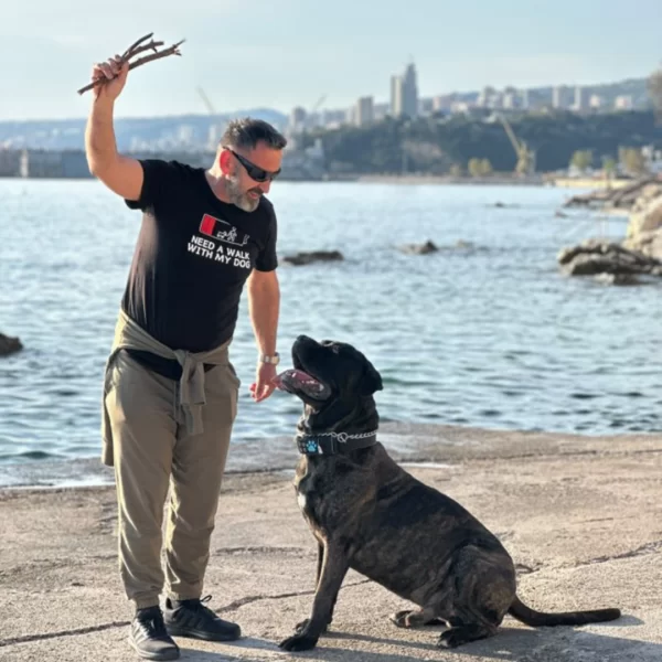 A man wearing a black t-shirt with a text "Need a walk with my dog" playing with his dog